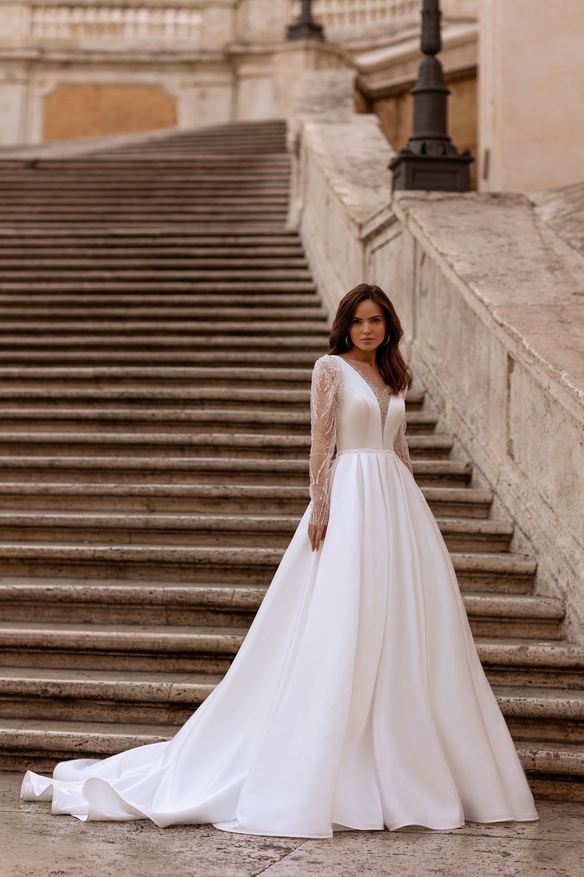 White A-line wedding dress with beaded illusion long sleeves, V-neckline, and a flowing train