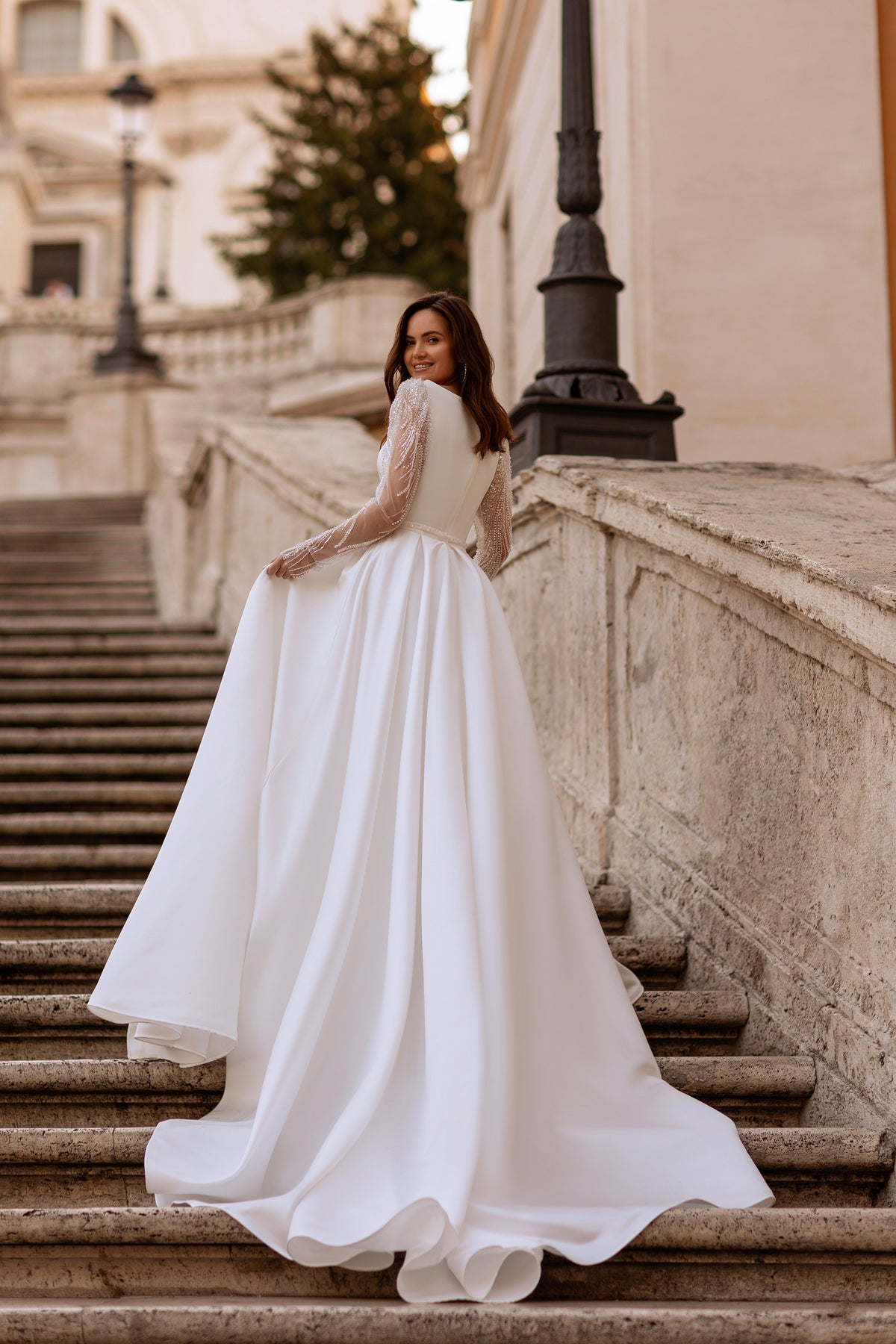 Back view of a white wedding dress with beaded sheer sleeves, a full skirt, and a sweeping train