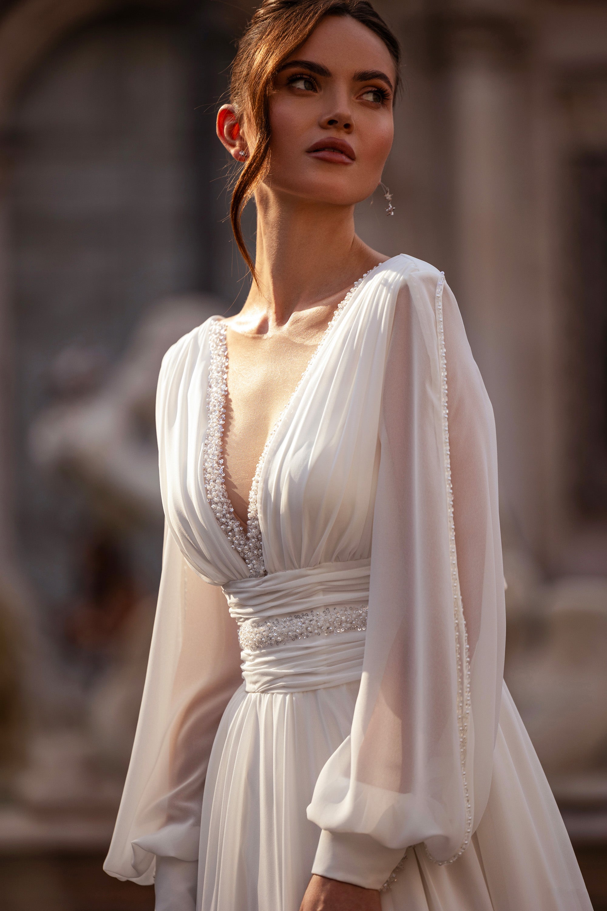 Close-up of an ivory wedding dress with gathered bishop sleeves, jeweled V-neckline, and ruched waist