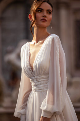 Close-up of an ivory wedding dress with gathered bishop sleeves, jeweled V-neckline, and ruched waist