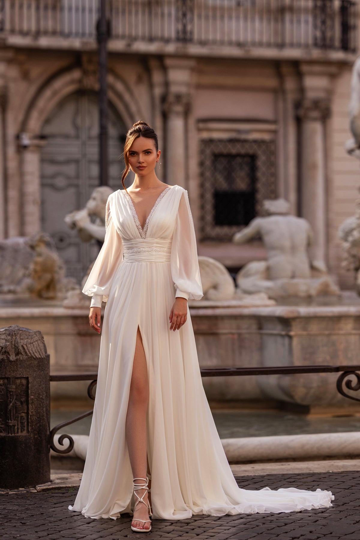 Ivory wedding dress with a deep V-neckline, long bishop sleeves, wrapped waist, and front slit
