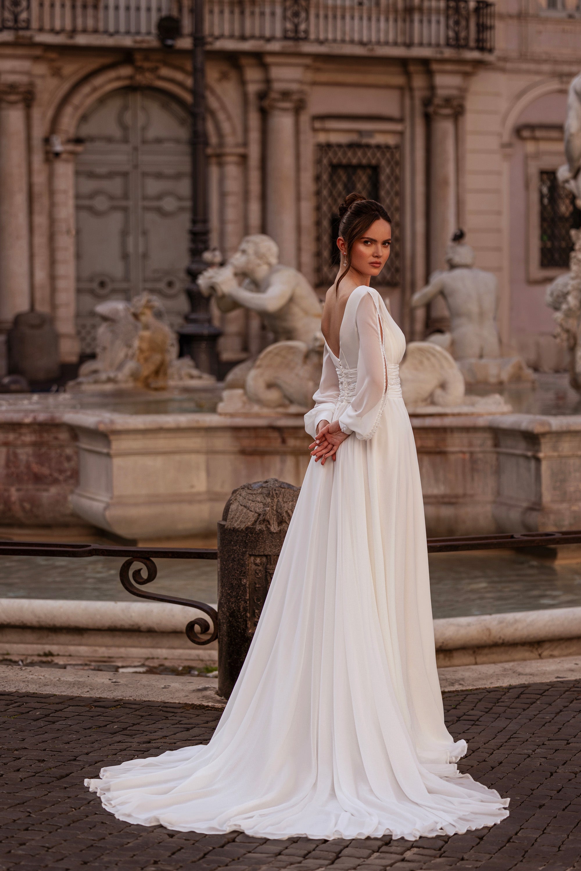 Flowing ivory wedding dress with long sheer sleeves, fitted waist, and an extended train
