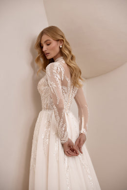 Side view of an ivory wedding dress with a V-shaped back, sheer lace sleeves, and beaded sheath skirt