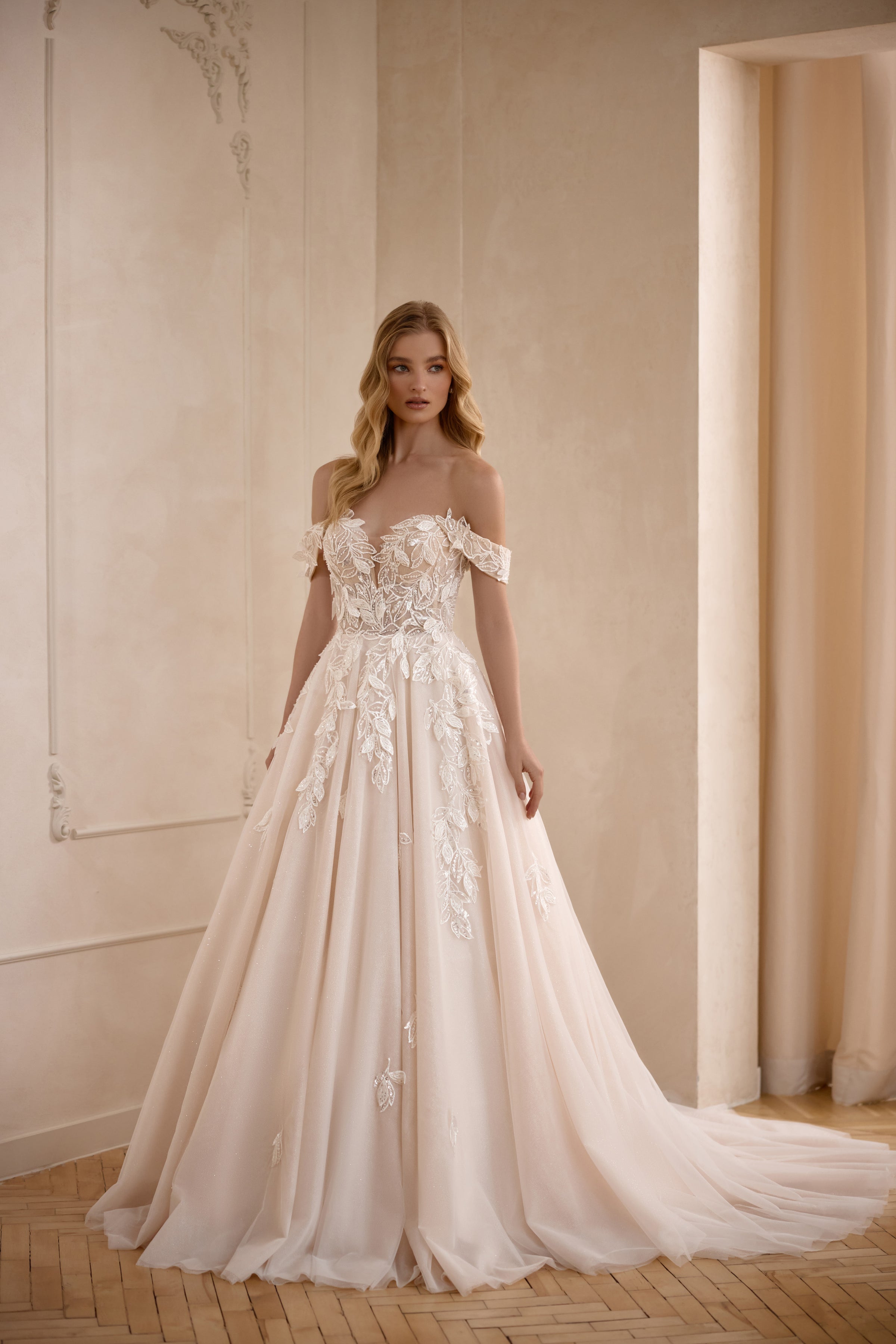 Ivory A-line wedding dress with an off-the-shoulder neckline, floral lace appliqués, and a sweeping train