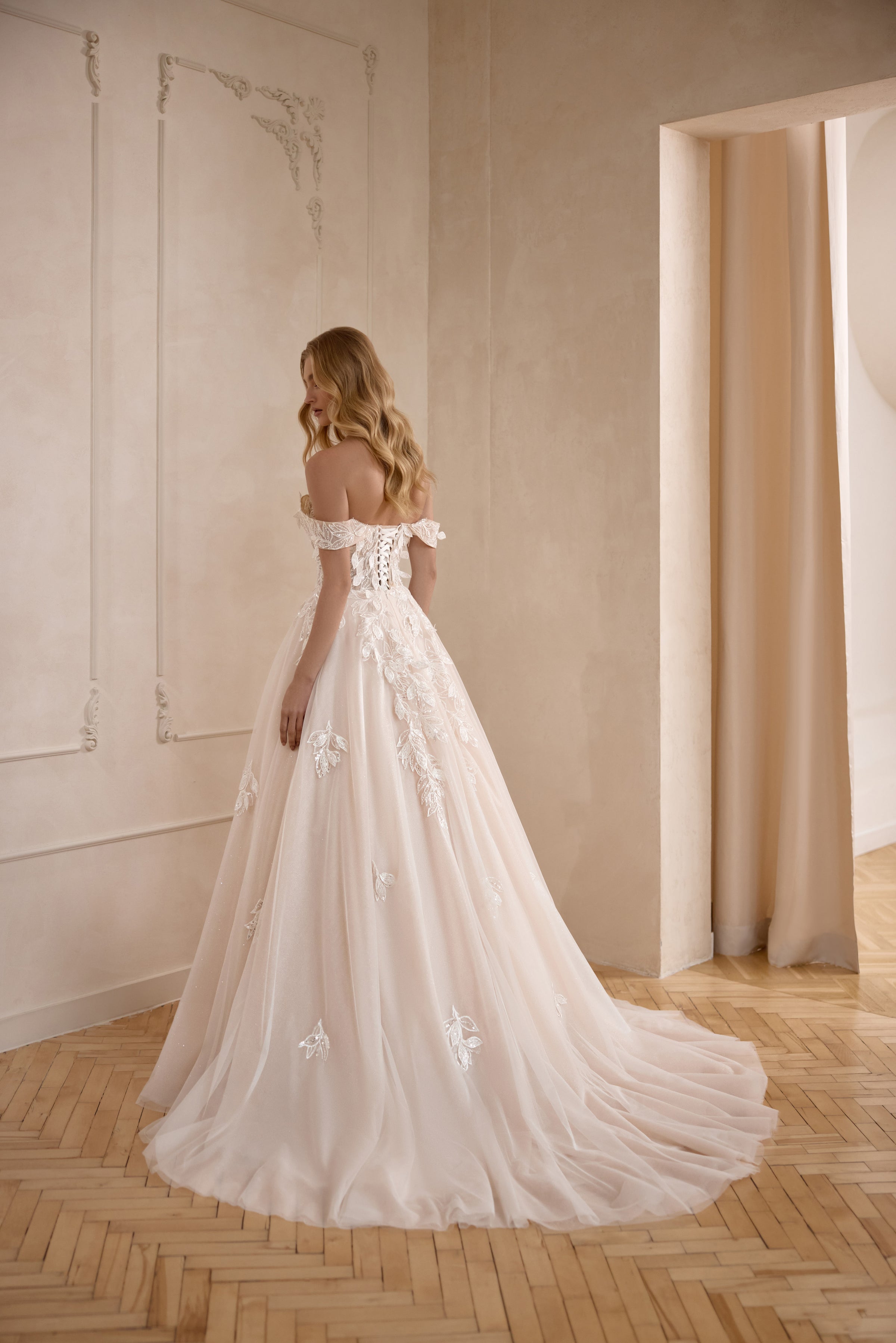 Open-back ivory A-line wedding dress with off-the-shoulder sleeves, floral lace accents, and a flowing train