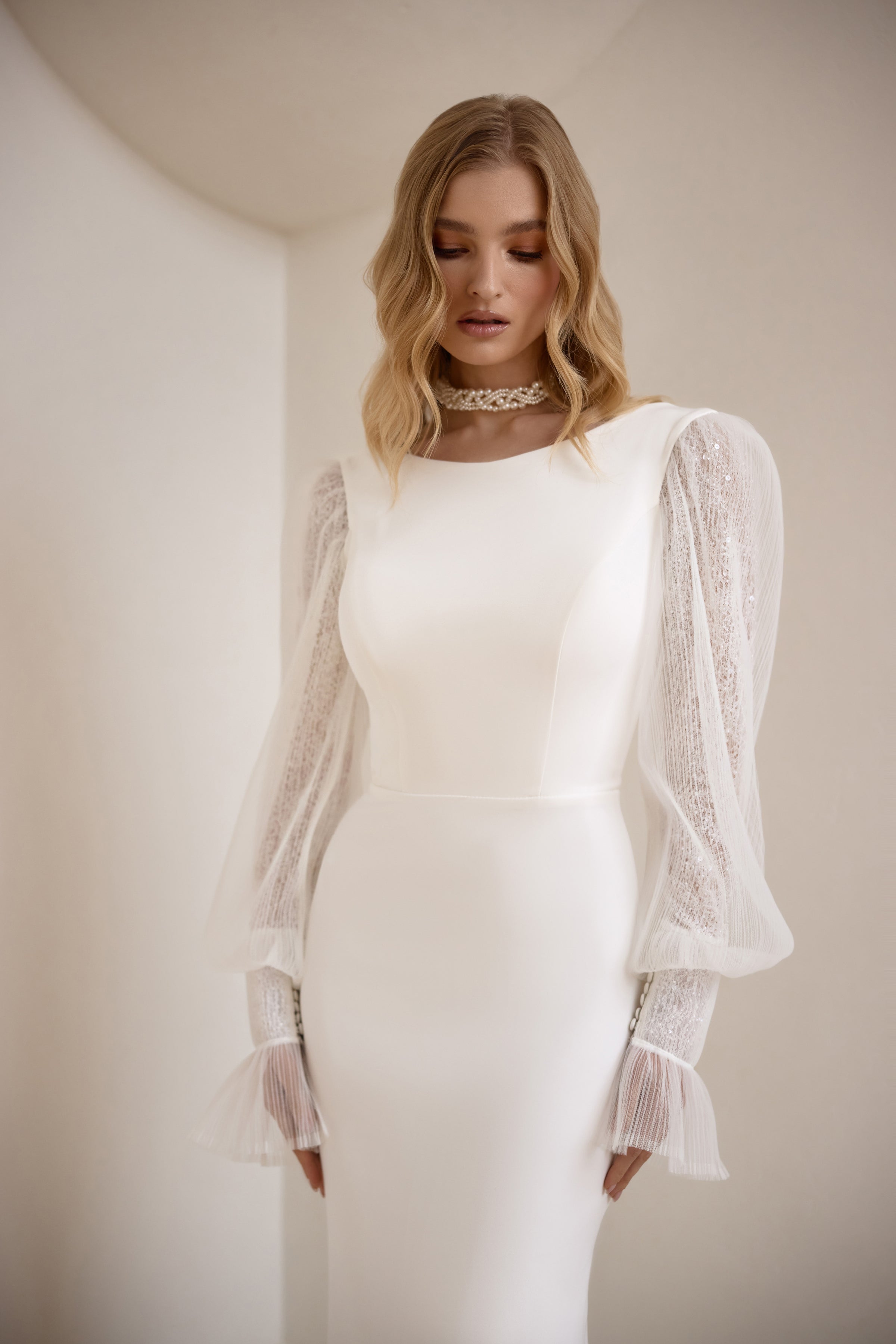 Close-up of an ivory wedding dress with a smooth boat neckline and sheer lace bishop sleeves
