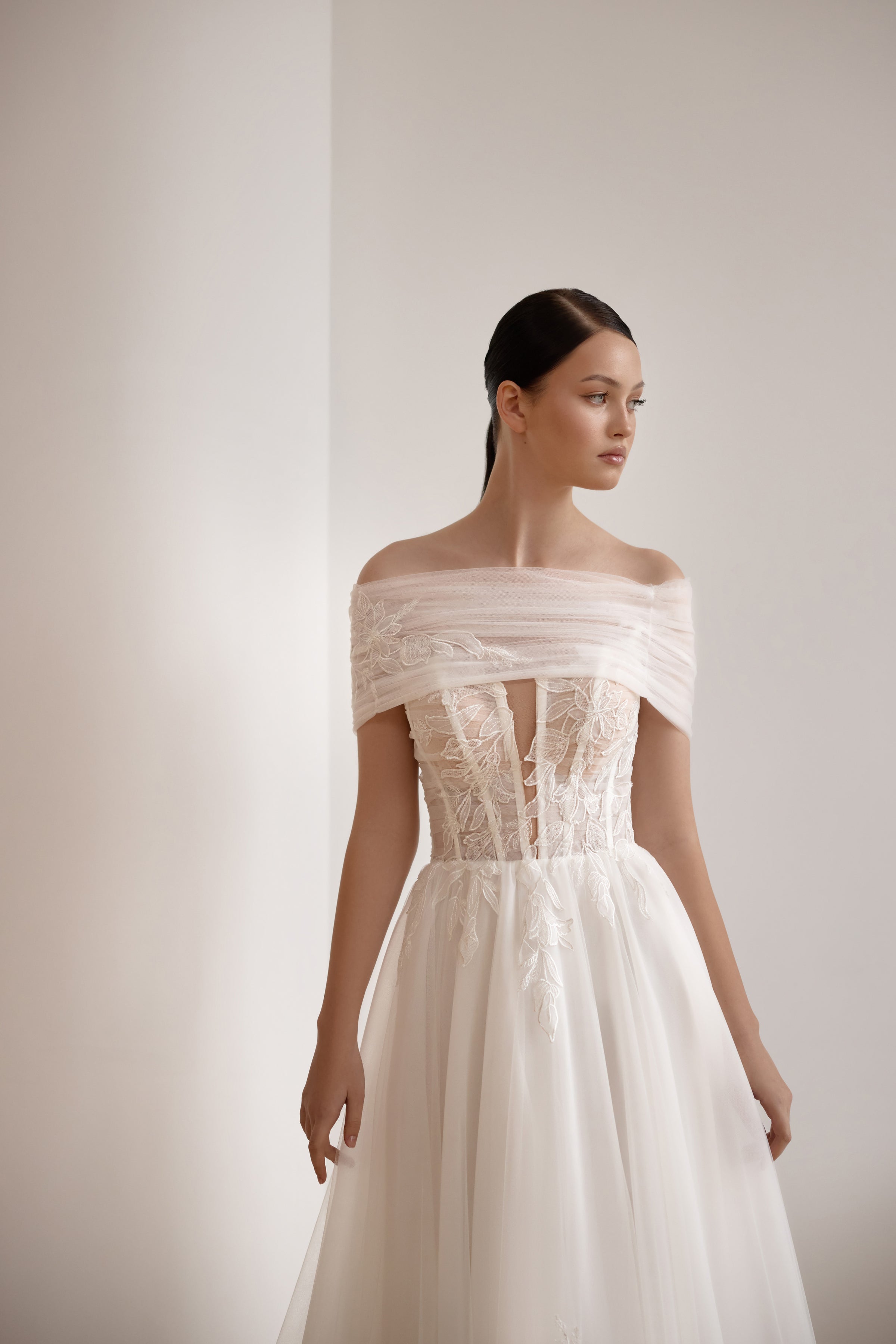 Ivory wedding dress featuring a draped off-the-shoulder neckline, corset-style lace bodice, and flowing A-line skirt
