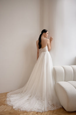 Open-back ivory wedding dress with a lace bodice, thin straps, flowing A-line skirt, and sweeping train