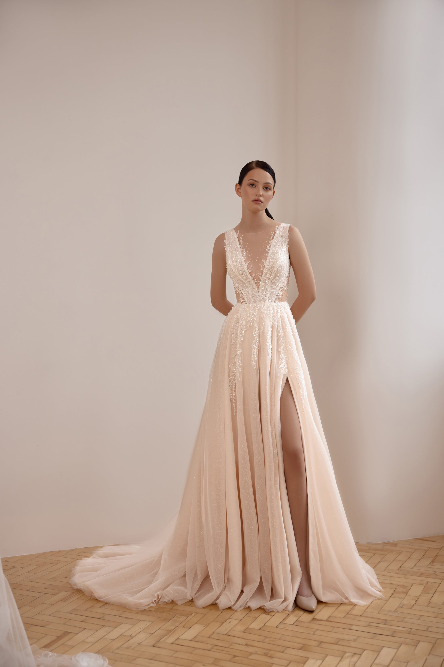 Blush A-line wedding dress with a deep illusion V-neck, sparkling lace, high slit, and flowing train