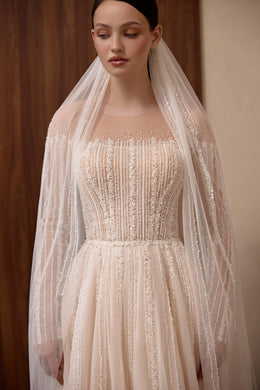 Close-up of a wedding dress bodice with dense vertical beadwork, sheer sleeves, and a straight neckline
