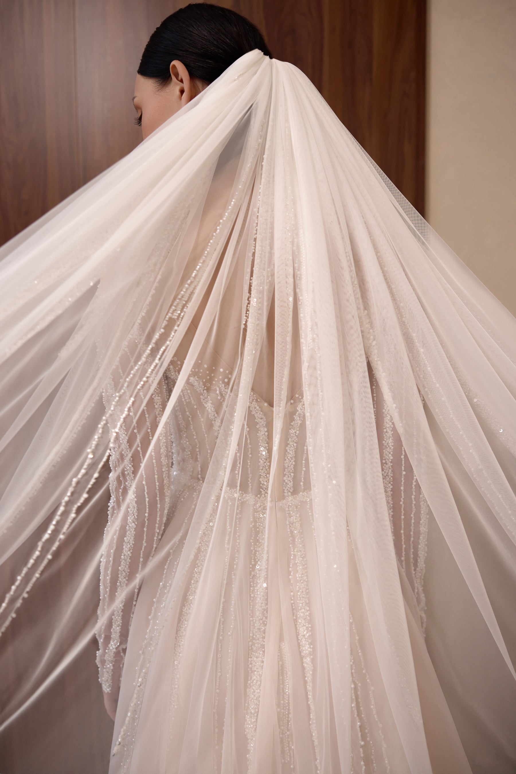 Sheer veil draped over the back of a beaded wedding dress with a flowing, textured train