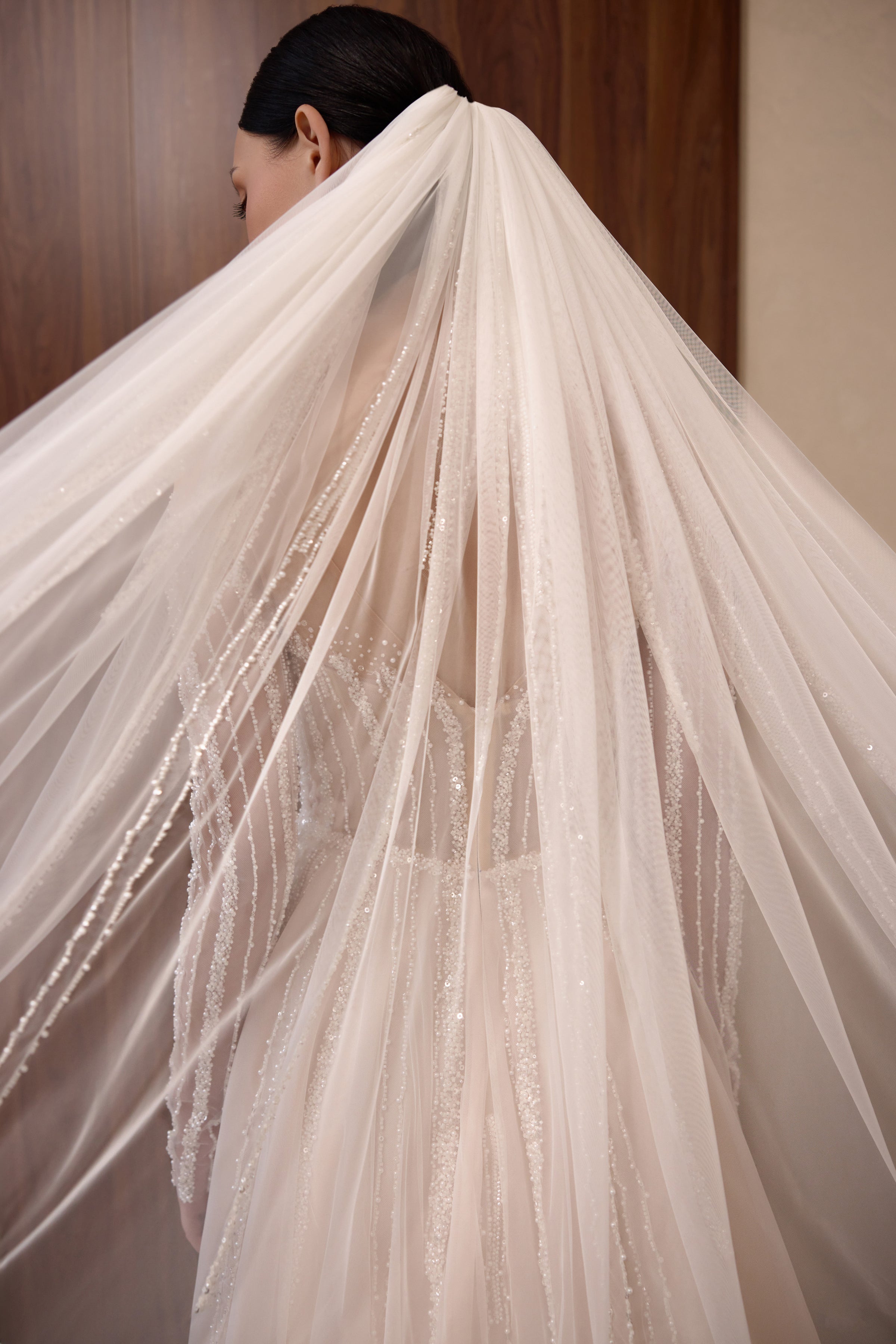 Sheer veil draped over the back of a beaded wedding dress with a flowing, textured train