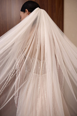 Sheer veil draped over the back of a beaded wedding dress with a flowing, textured train