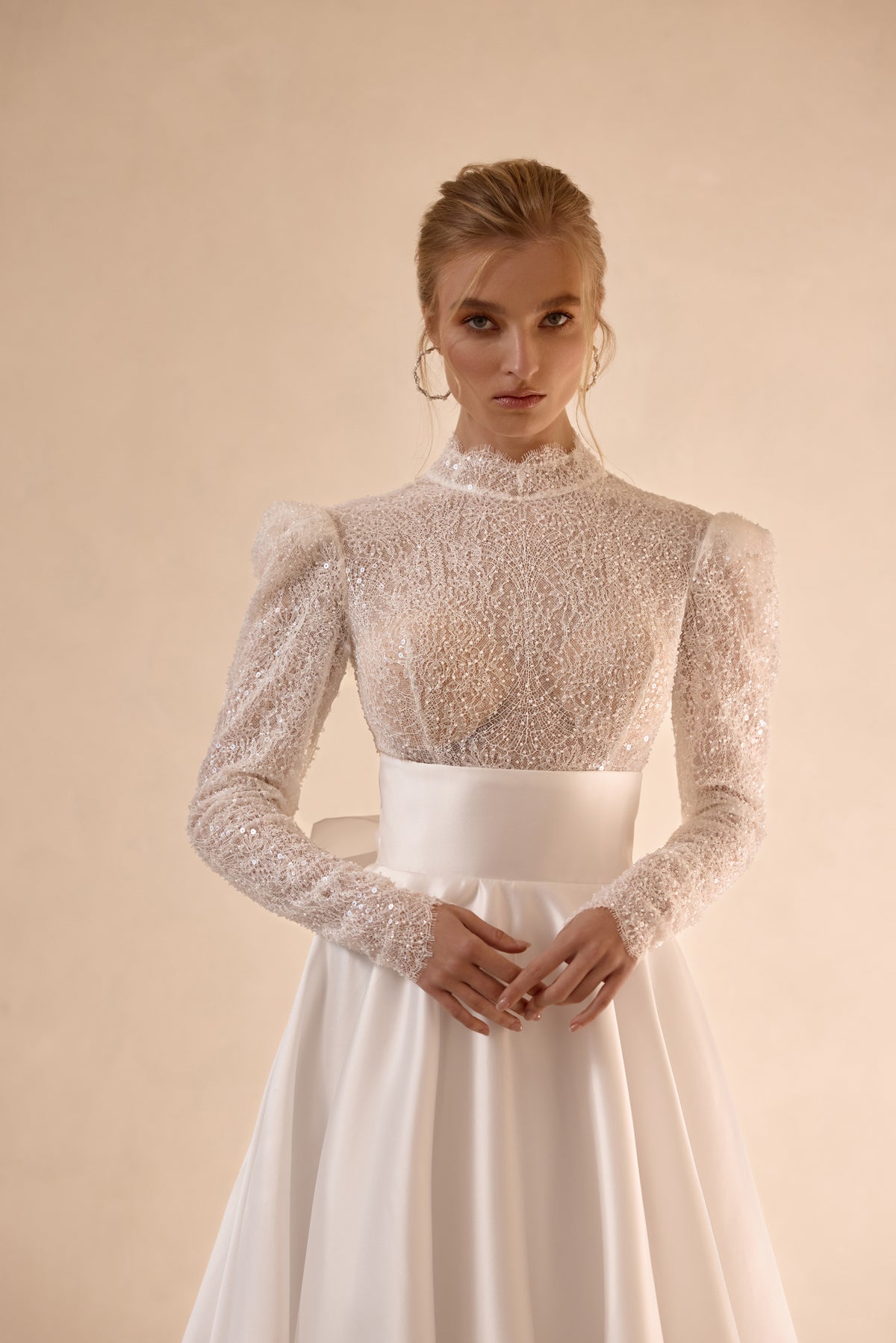 Close-up of an ivory wedding dress with a high neckline, sheer beaded bodice, puff shoulders, and long sleeves