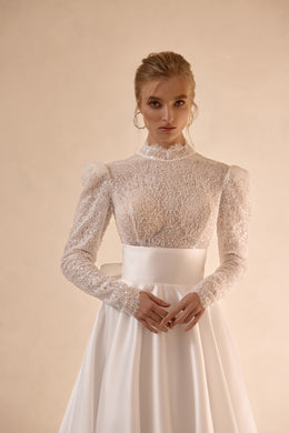 Close-up of an ivory wedding dress with a high neckline, sheer beaded bodice, puff shoulders, and long sleeves