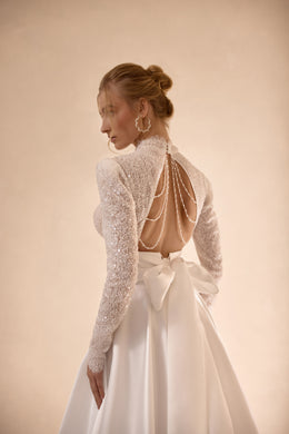 Open back with delicate beaded straps and a large waist bow on an ivory wedding dress with long sleeves