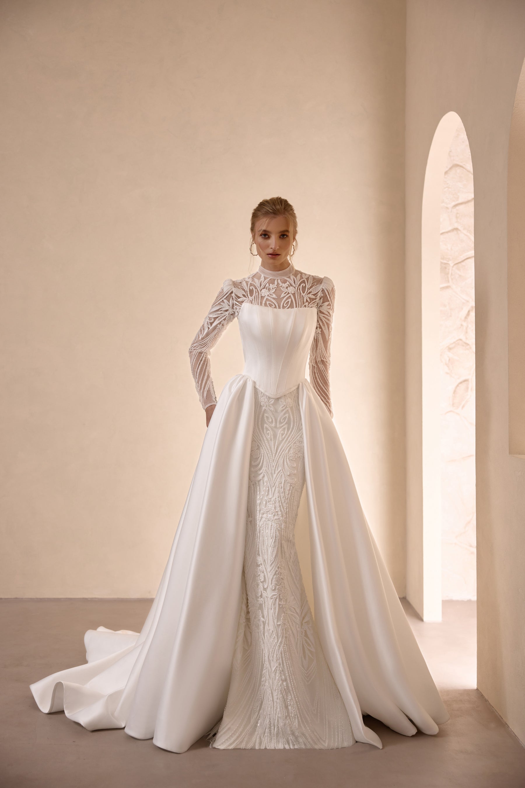 Ivory high-neck wedding dress with long lace sleeves, fitted bodice, and flowing satin overskirt