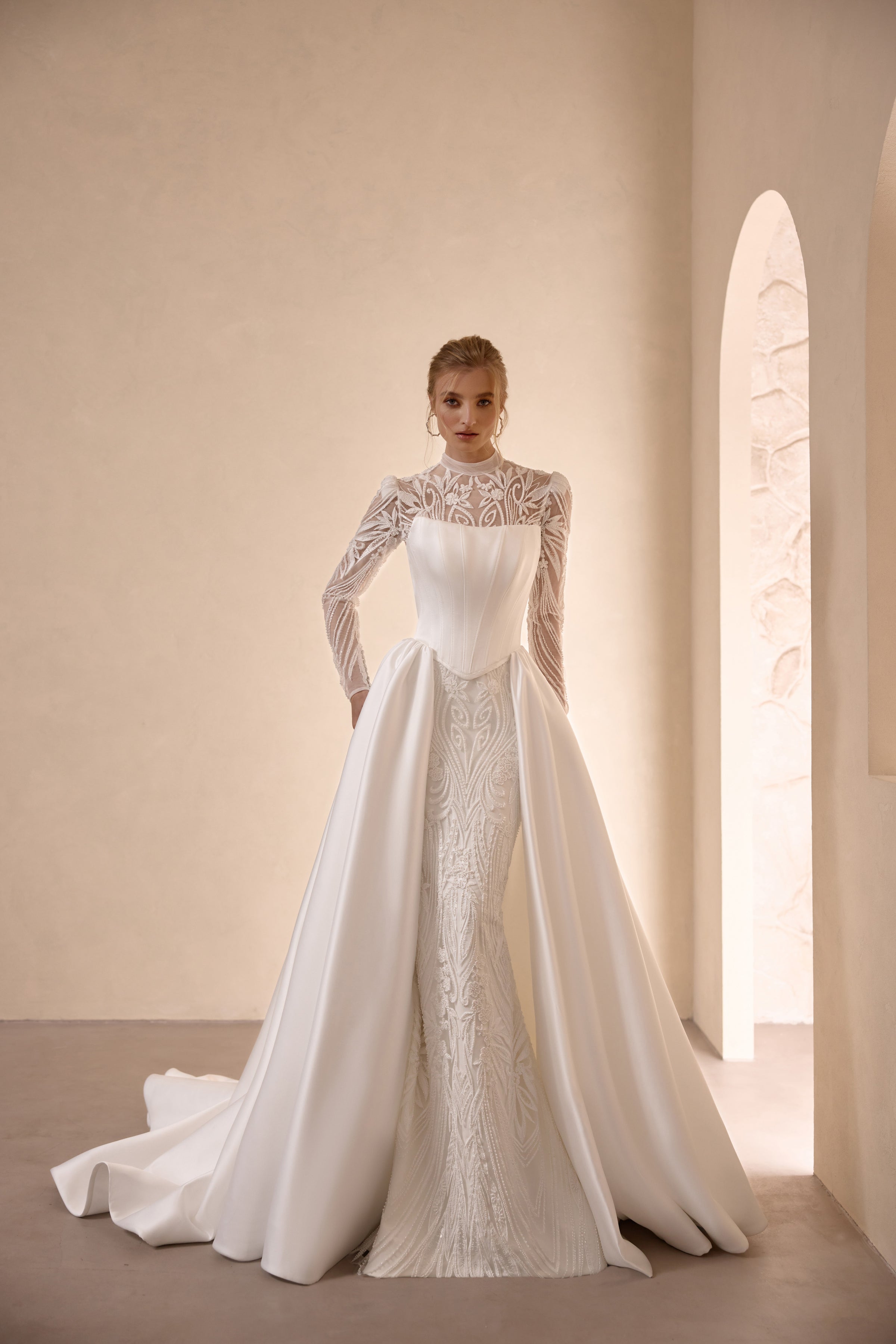 Ivory high-neck wedding dress with long lace sleeves, fitted bodice, and flowing satin overskirt