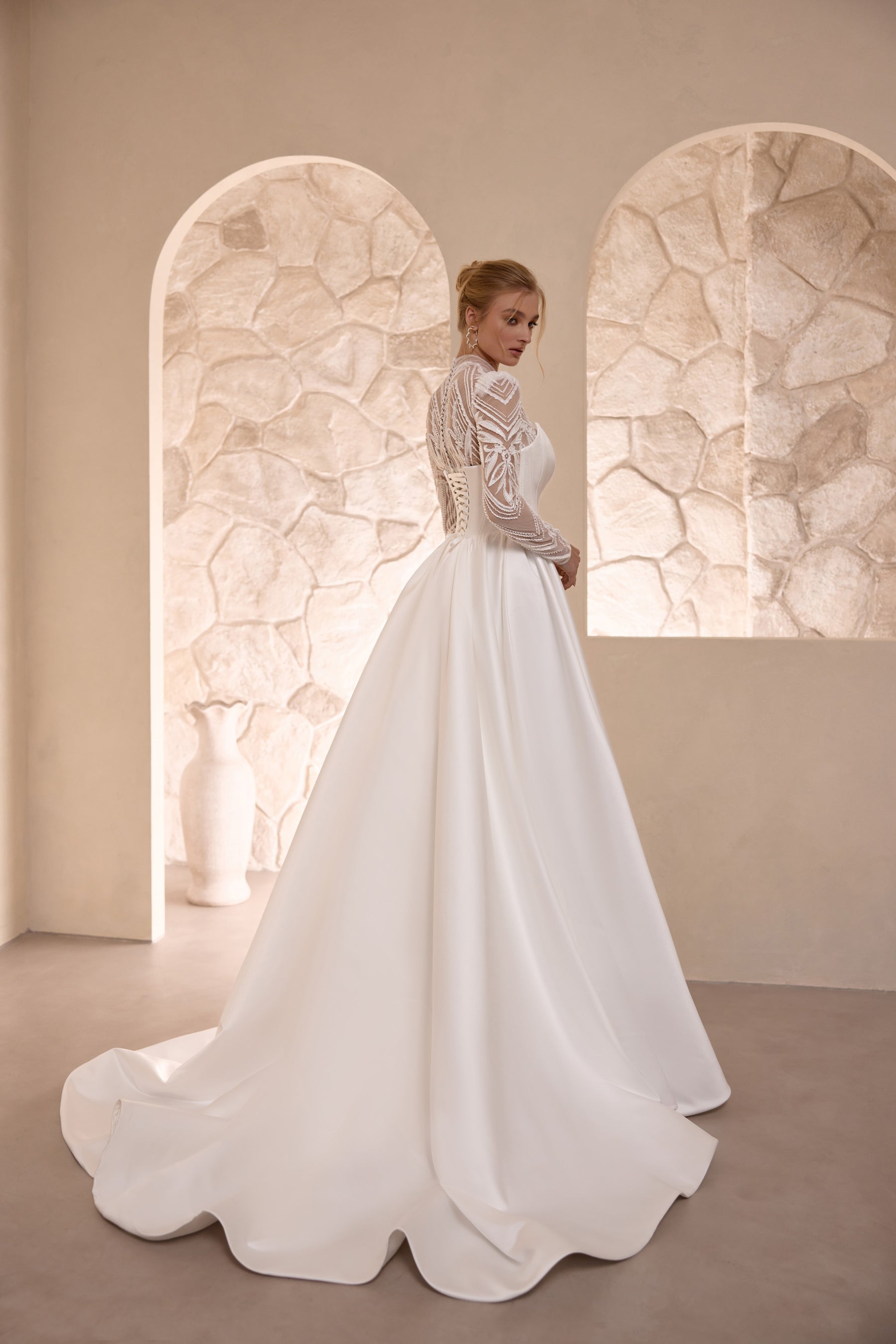 Three-quarter back view of an ivory wedding dress with lace sleeves and a sweeping satin train