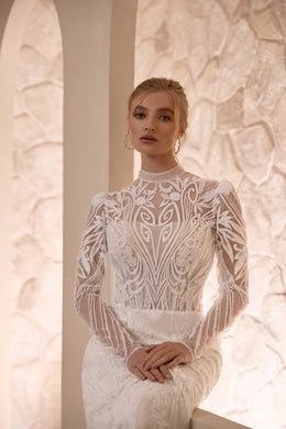 Close-up of an ivory wedding dress with intricate floral lace, high neckline, and long sheer sleeves