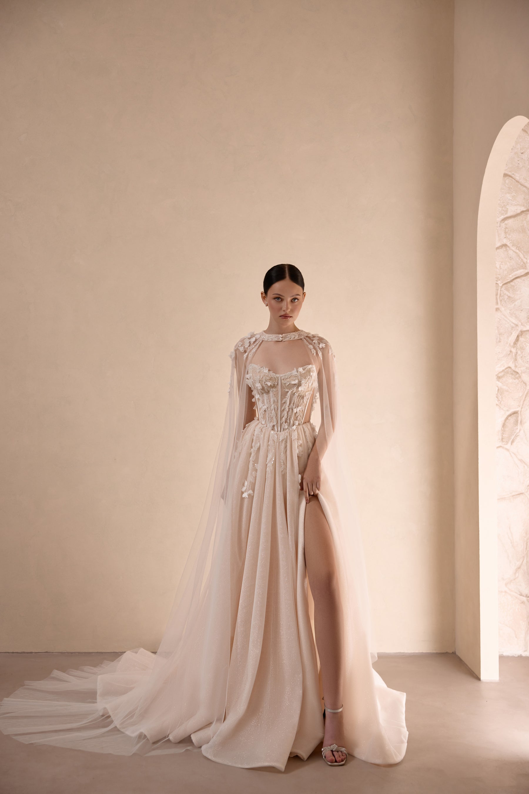 Ivory wedding dress with a beaded corset bodice, high slit, and sheer flowing cape