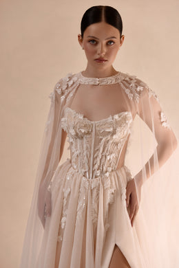 Ivory wedding dress with a jeweled corset bodice, sheer floral cape, and high front slit
