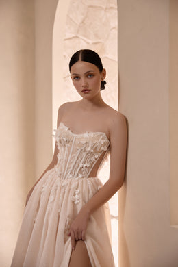 Strapless ivory wedding dress featuring a floral-embellished corset and high skirt slit