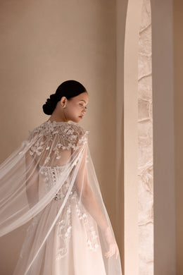 Close-up of a sheer floral-embroidered cape draped over an ivory wedding dress