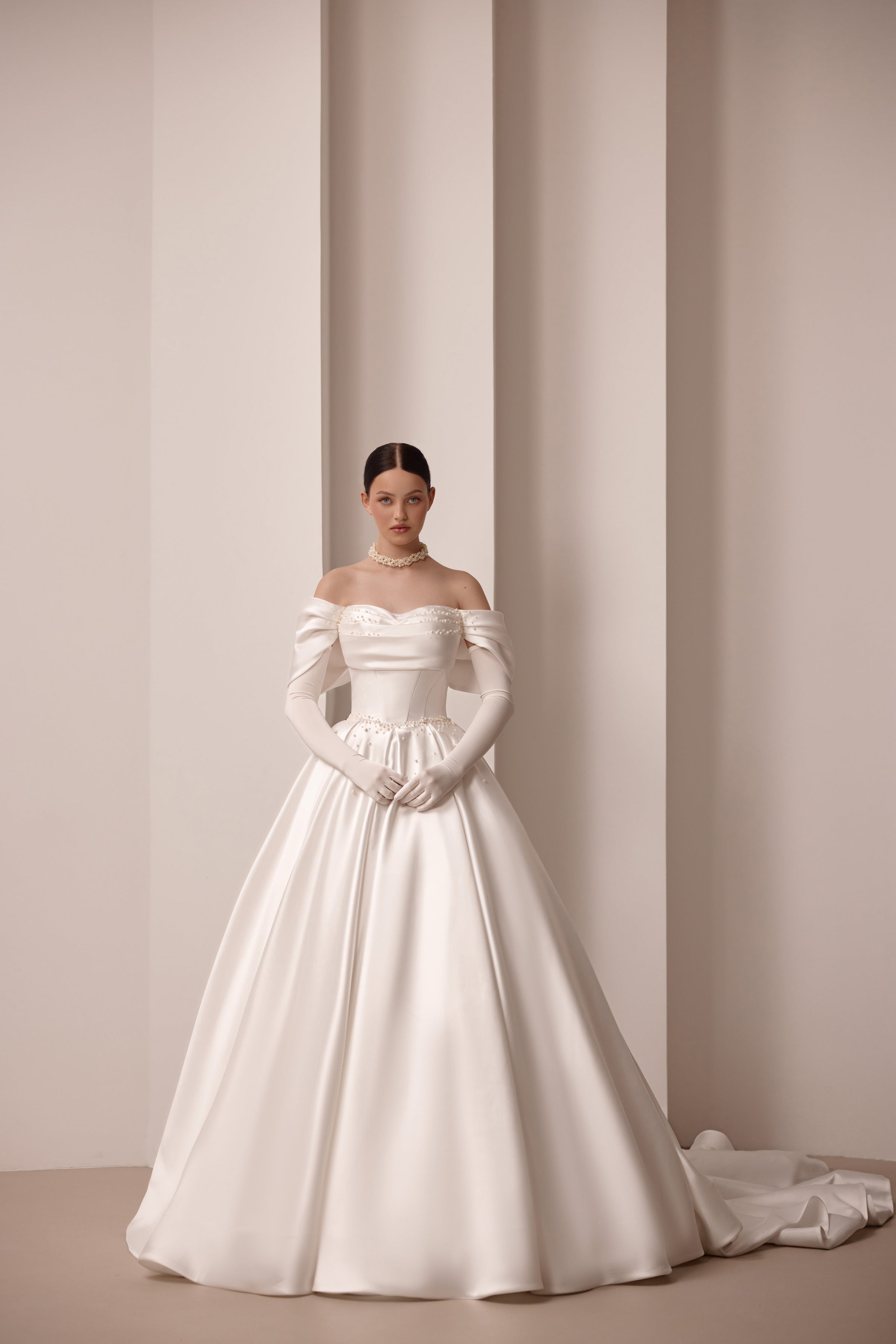 Ivory satin ball gown wedding dress with an off-the-shoulder neckline, fitted sleeves, and long train