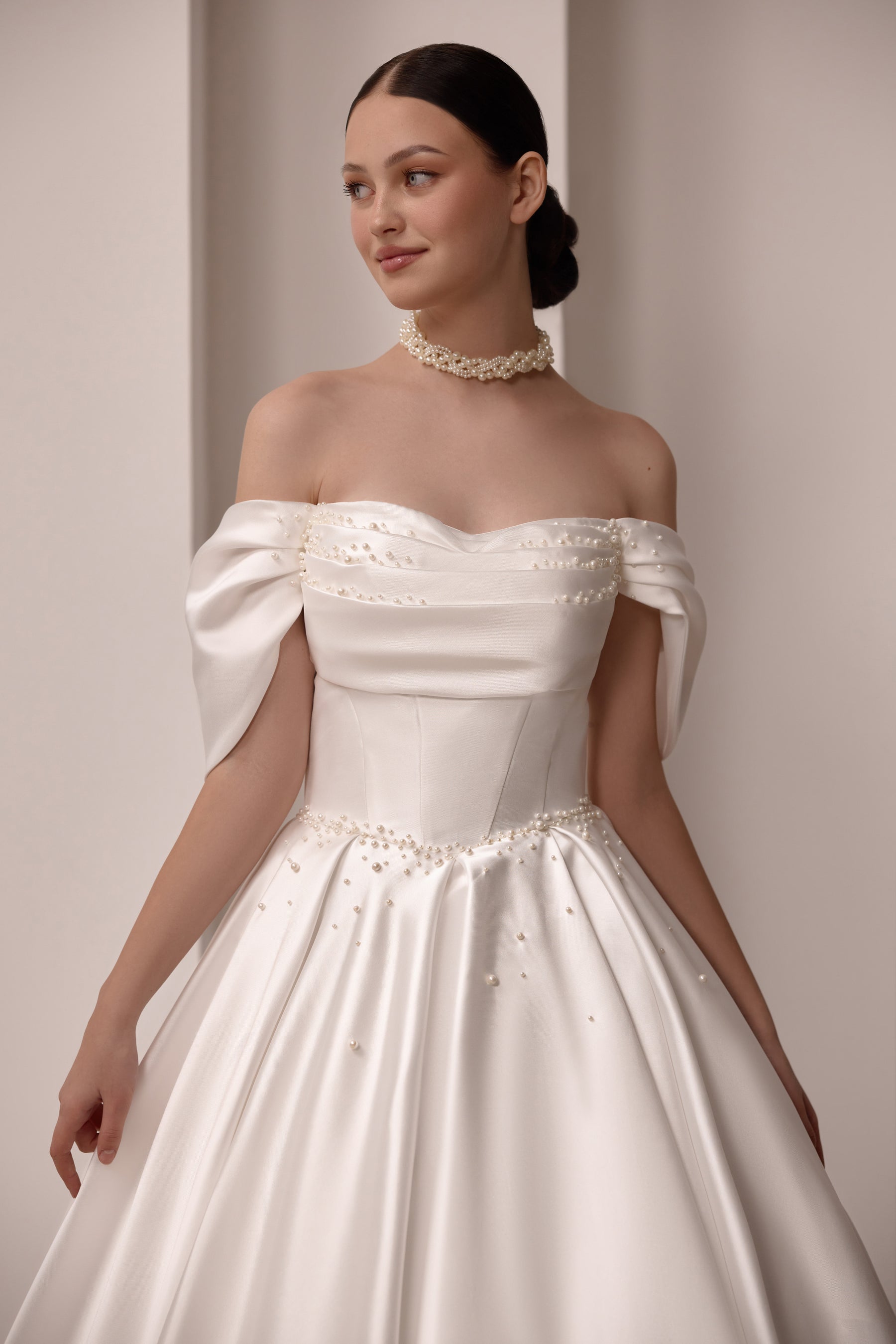 Close-up of an ivory wedding dress with an off-the-shoulder neckline, gathered bodice, and pearl embellishments