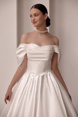 Close-up of an ivory wedding dress with an off-the-shoulder neckline, gathered bodice, and pearl embellishments