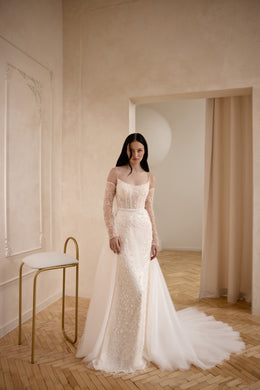 Ivory beaded sheath wedding dress with square neckline, sheer long sleeves, and a flowing overskirt