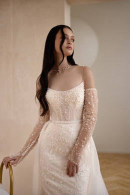 Close-up of the beaded bodice, square neckline, and sheer long sleeves on an ivory wedding dress