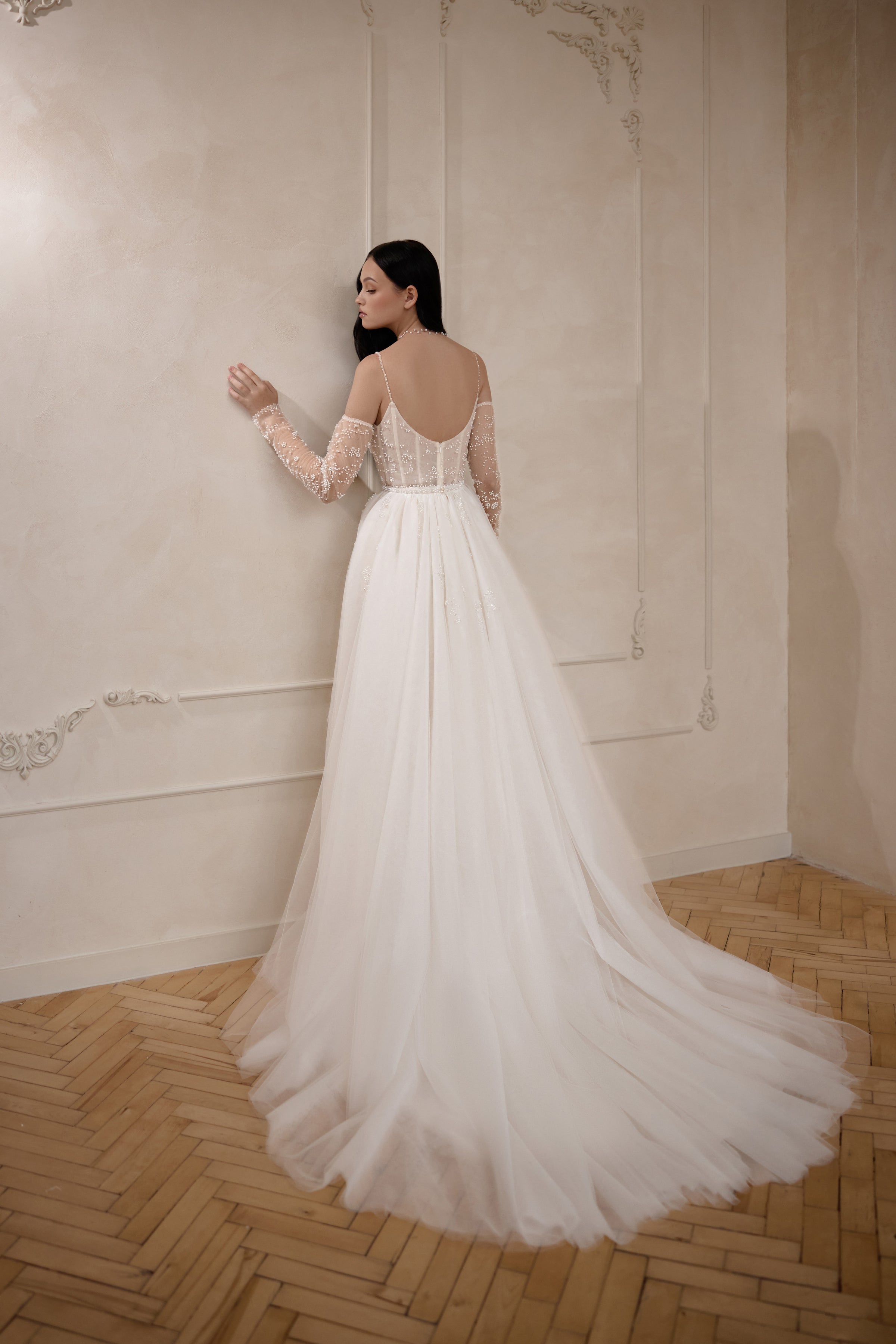Open scoop back with sheer sleeves and a full tulle train on an ivory wedding dress