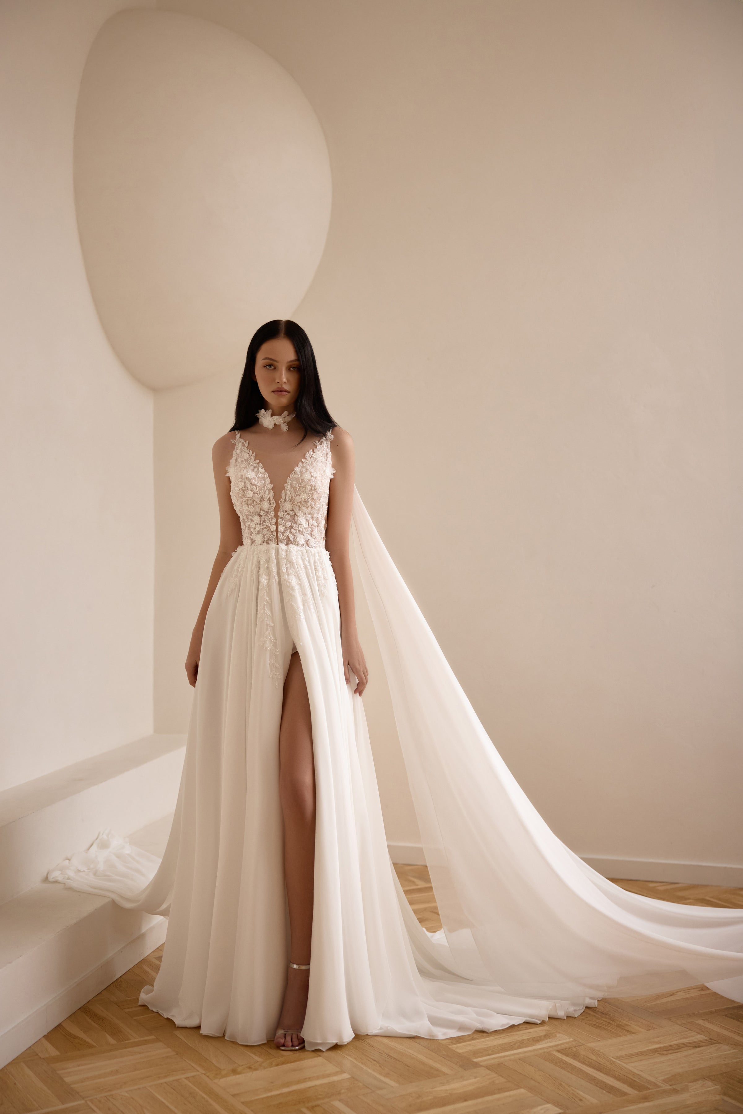 Ivory A-line wedding dress with floral lace bodice, deep V-neckline, high slit, and flowing cape