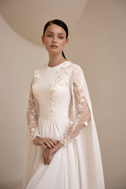 Close-up of an ivory wedding dress with a high neckline, floral lace sleeves, lace appliqués, and cape
