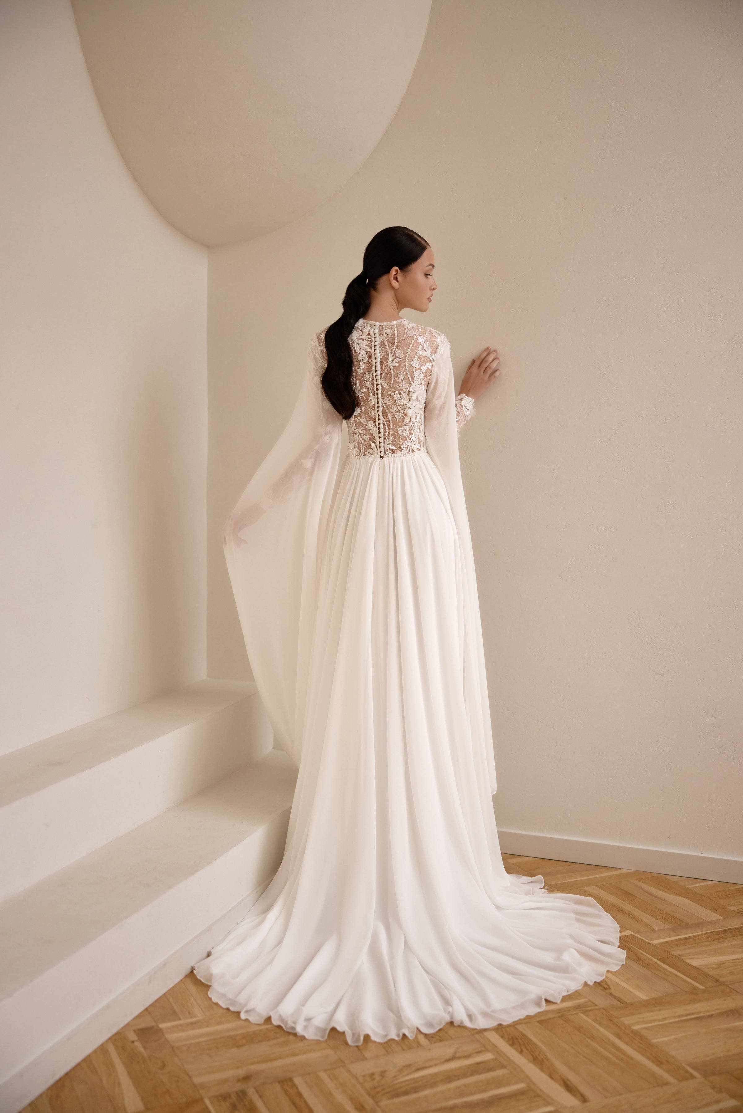 Back of an ivory wedding dress showing a lace-covered bodice, flowing cape, gathered skirt, and train