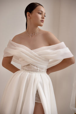 Close-up of an ivory wedding dress showing the draped off-the-shoulder neckline, beaded waist, and high slit