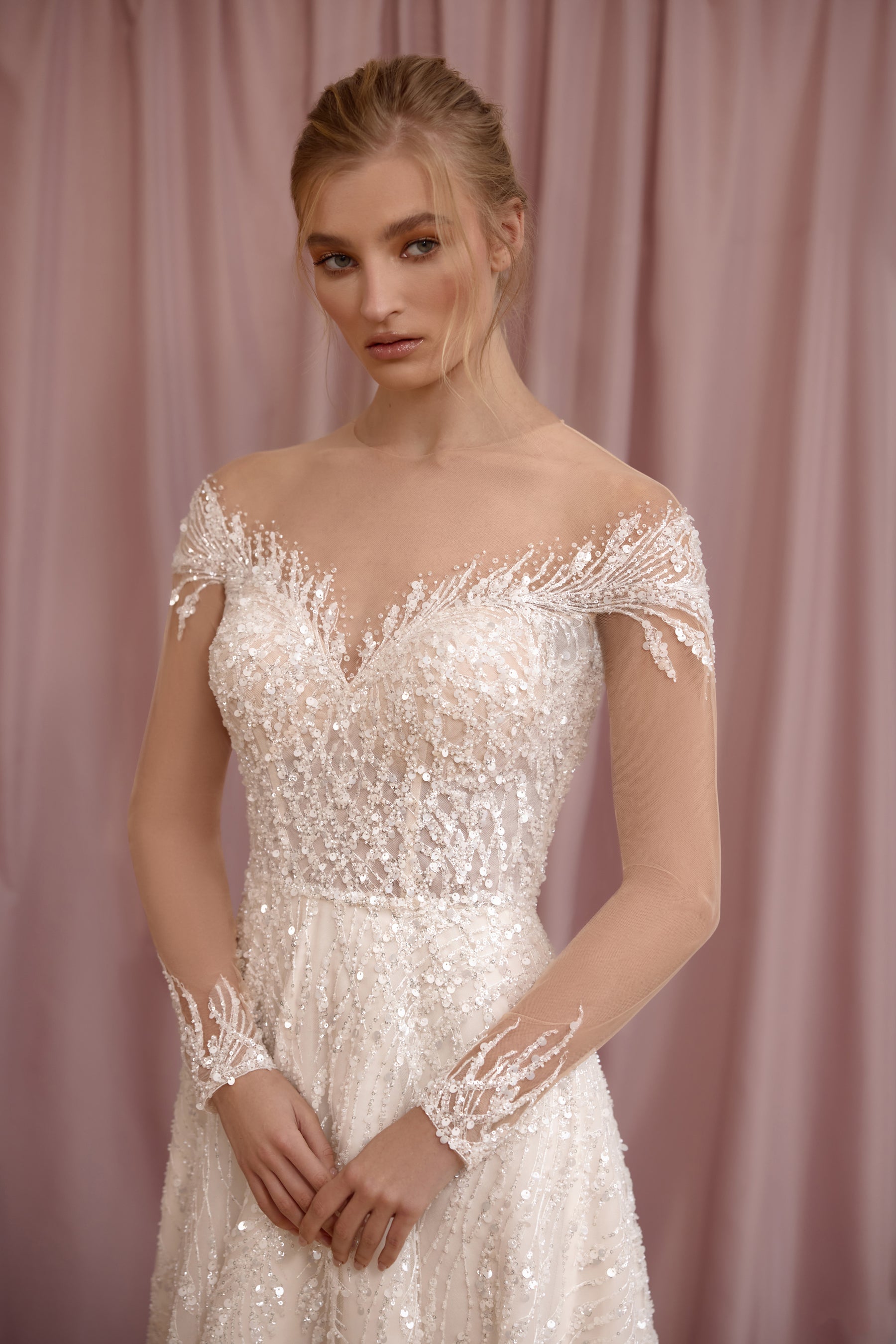 Close-up of an ivory wedding dress bodice with an off-the-shoulder illusion neckline, beaded lace, and long sheer sleeves