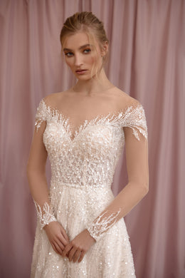 Close-up of an ivory wedding dress bodice with an off-the-shoulder illusion neckline, beaded lace, and long sheer sleeves