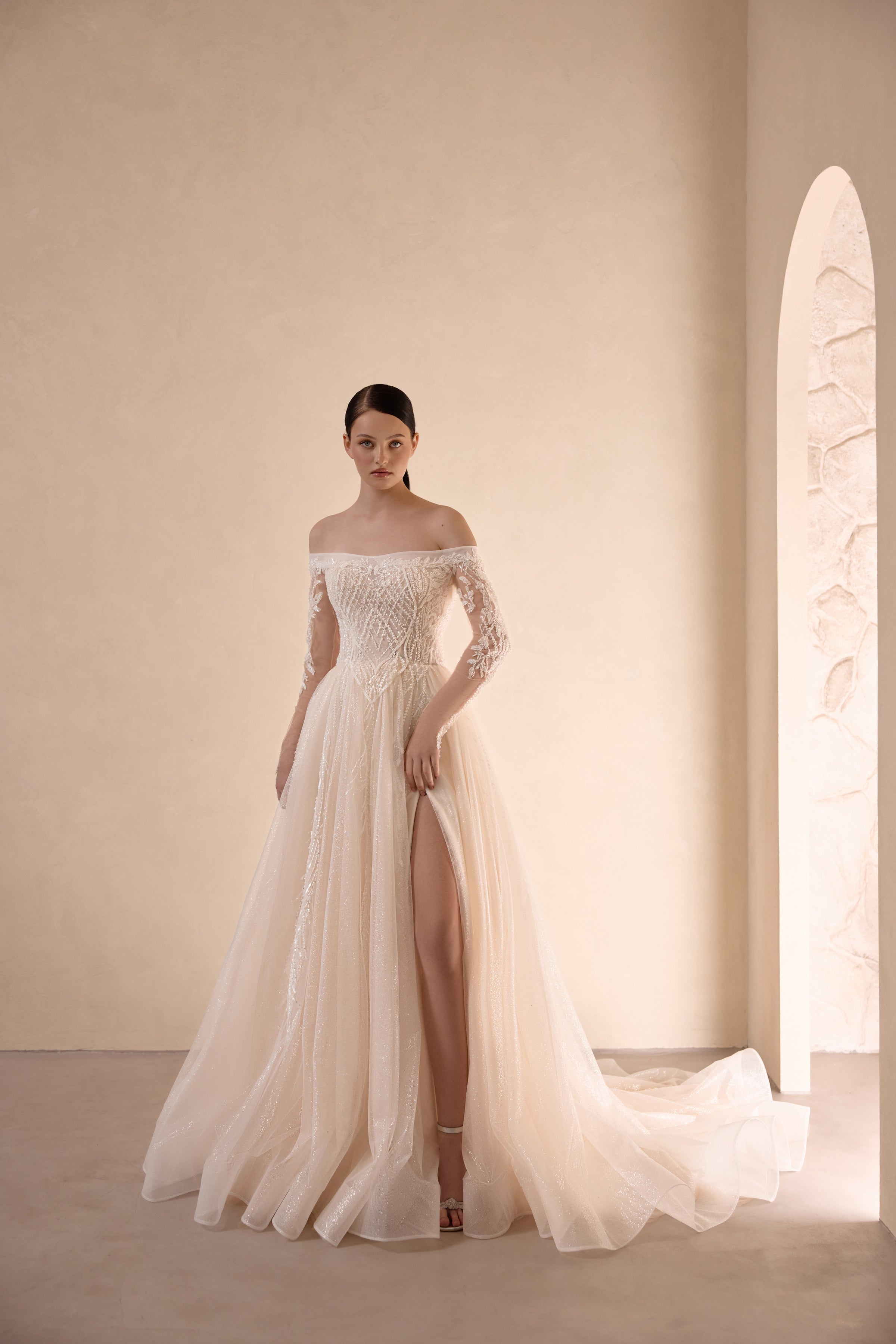 Ivory A-line wedding dress with an off-the-shoulder neckline, sheer floral sleeves, slit, and train