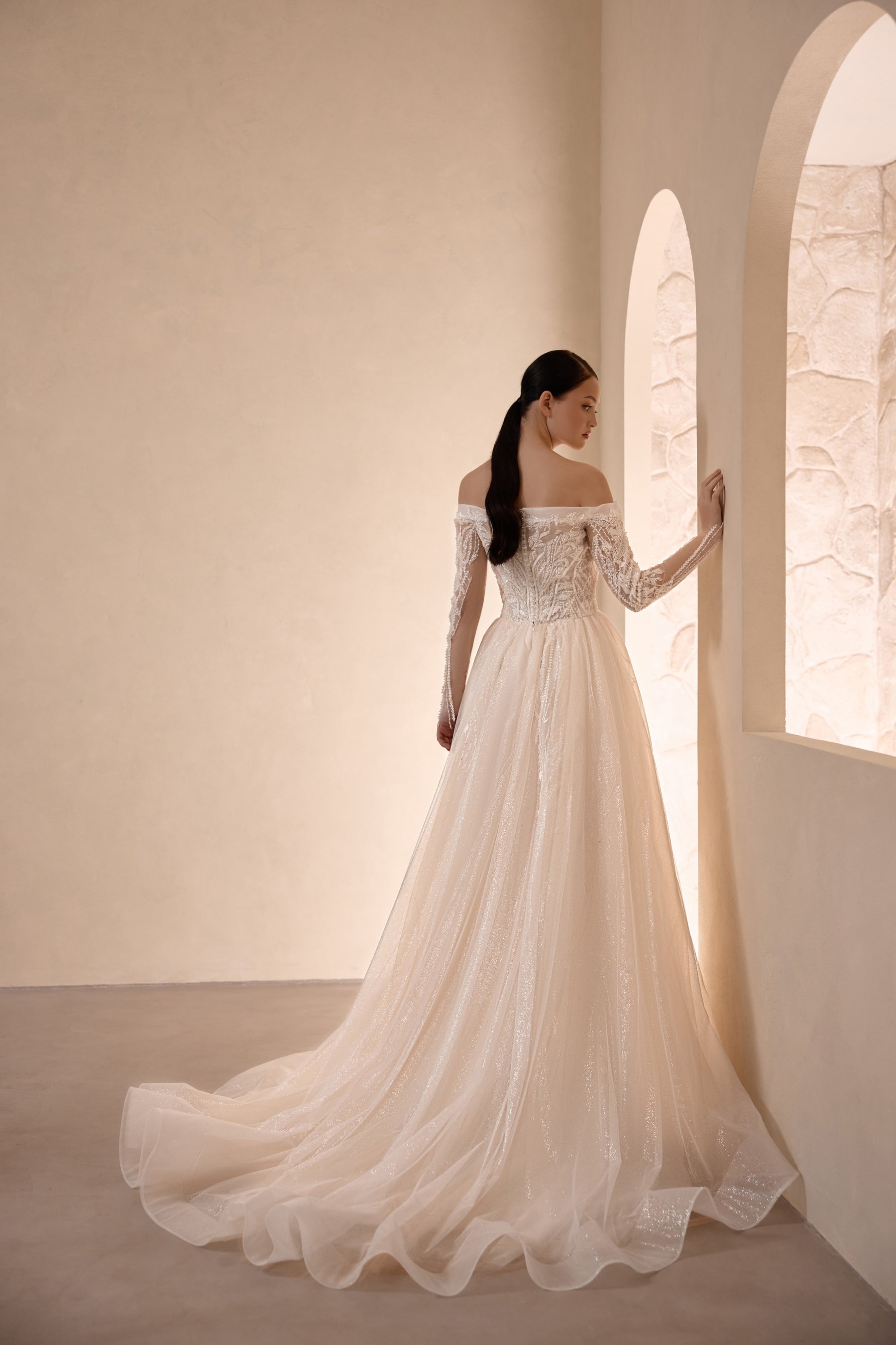 Ivory wedding dress with a beaded off-the-shoulder back, long sleeves, and sweeping train