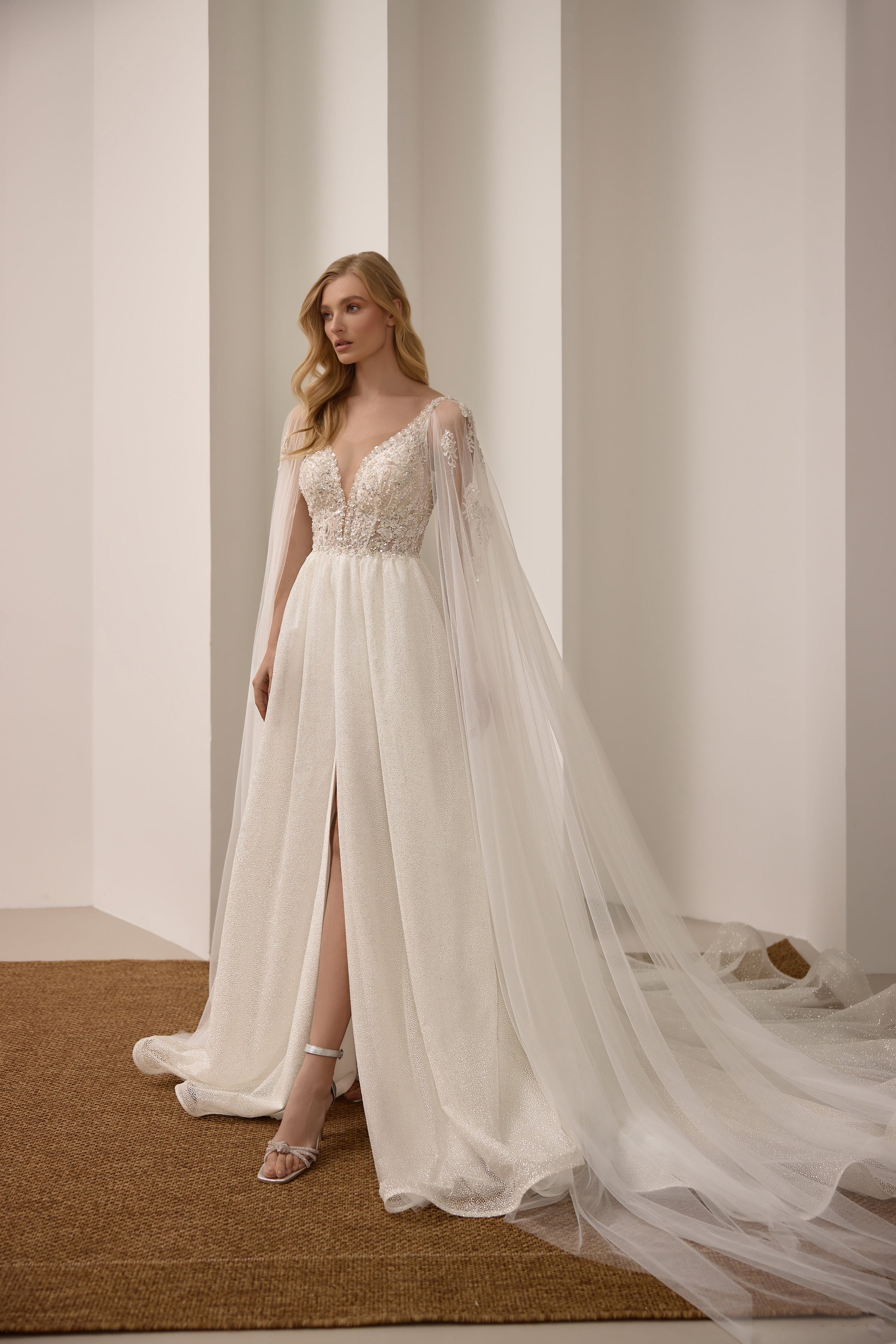 Sparkling ivory A-line wedding dress with a deep V-neck, front slit, and flowing sheer cape