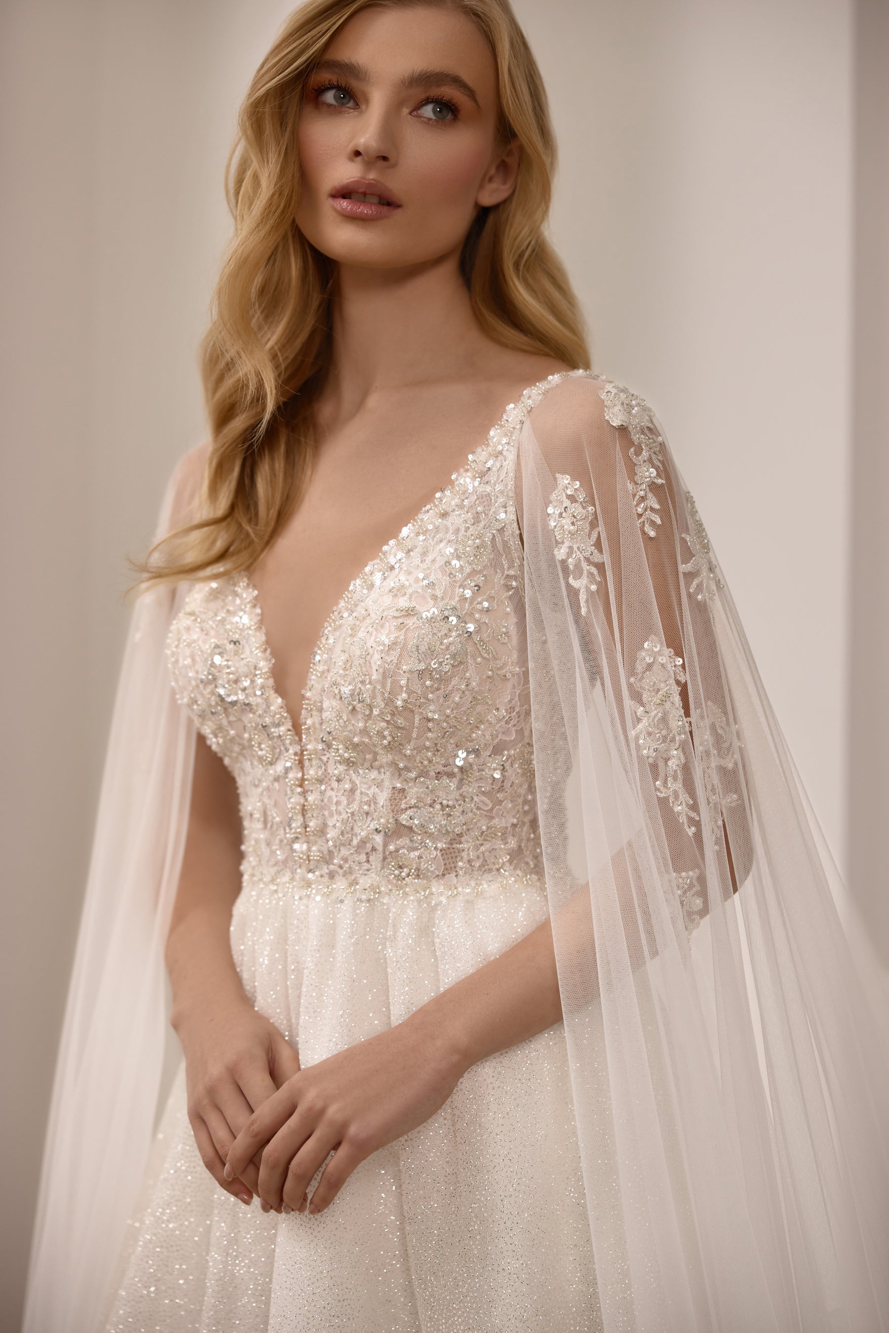 Close-up of a beaded V-neck bodice and sheer glitter sleeves on an ivory wedding dress