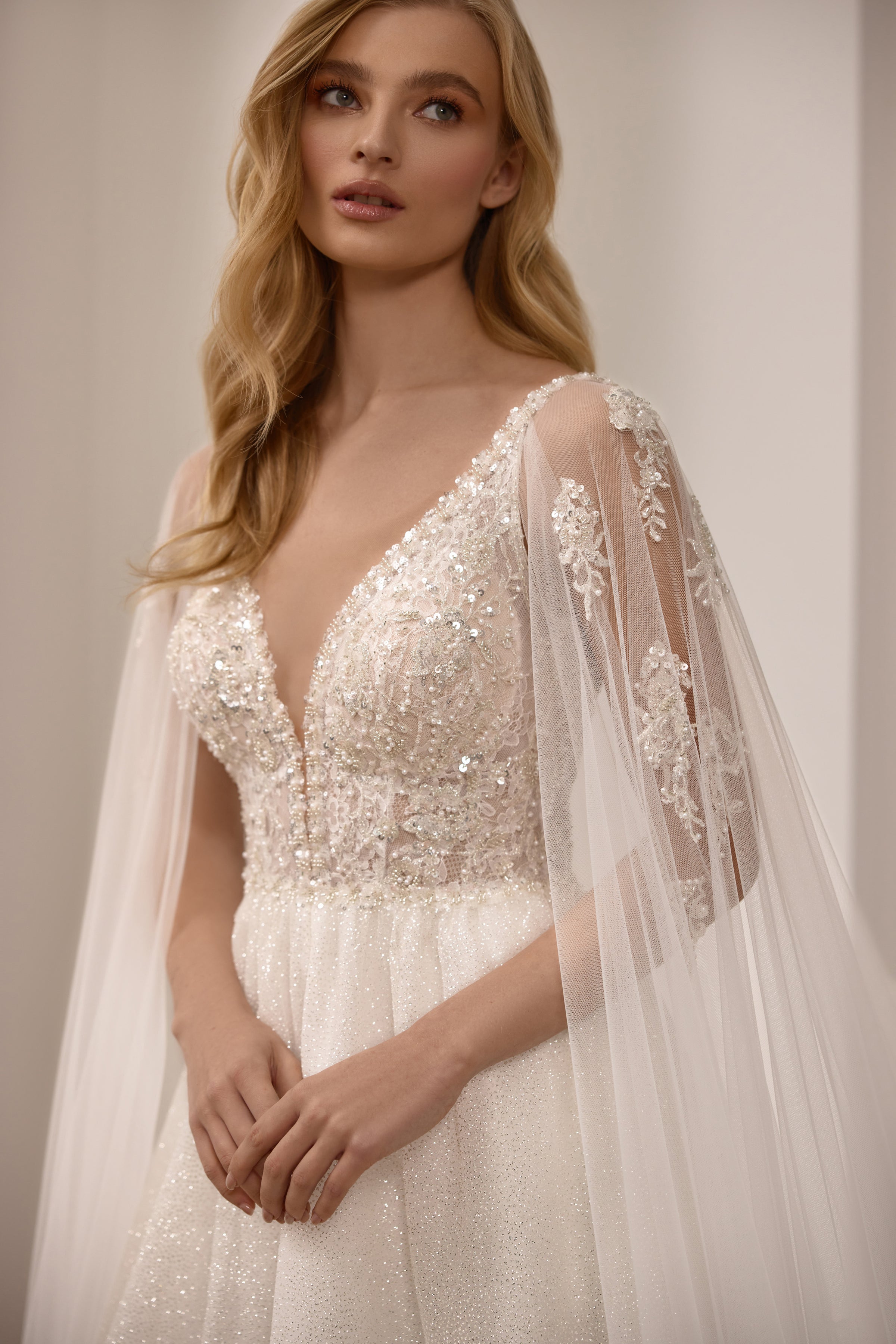 Close-up of a beaded V-neck bodice and sheer glitter sleeves on an ivory wedding dress