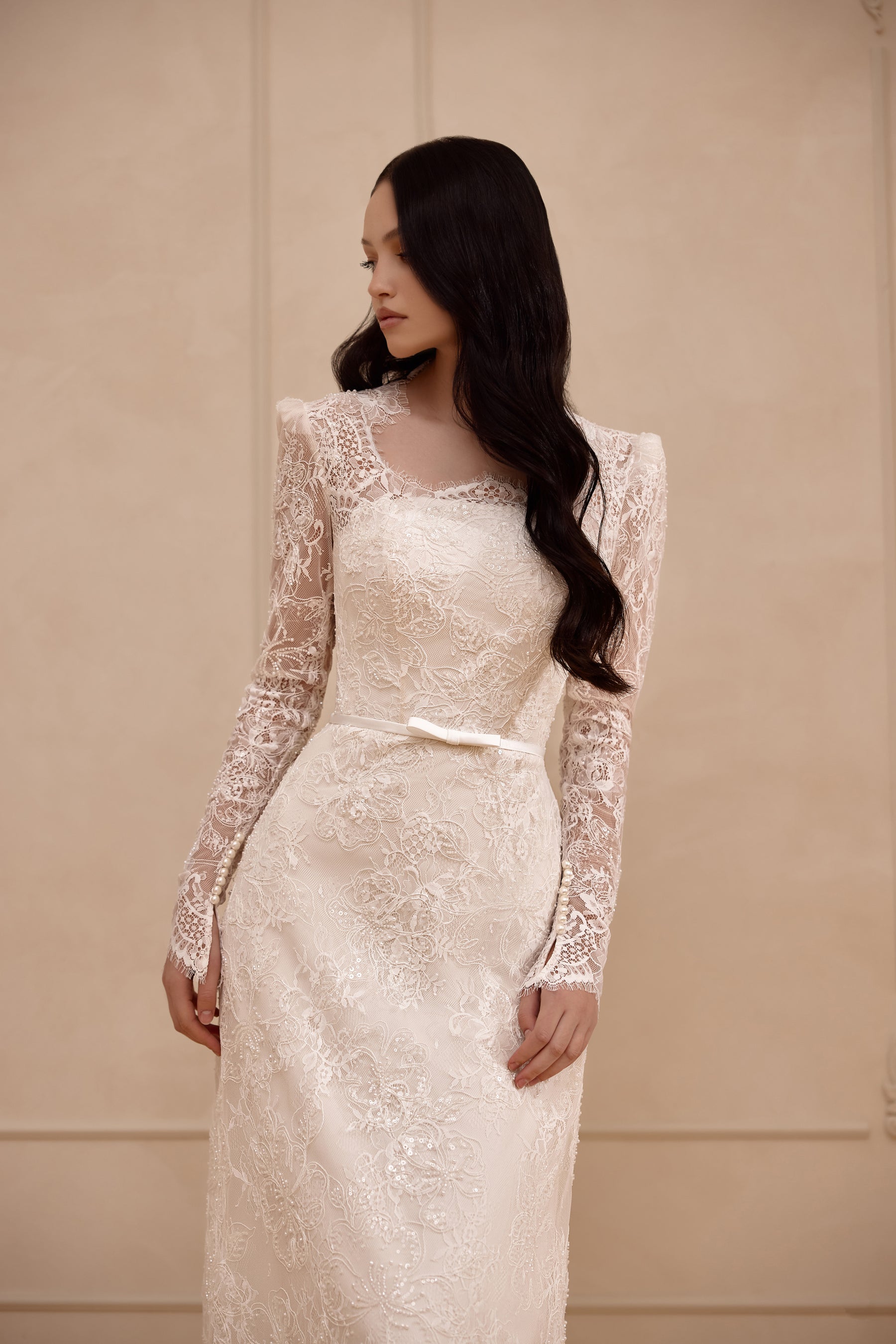 Close-up of an ivory wedding dress bodice with floral lace, sheer long sleeves, and a softly rounded neckline