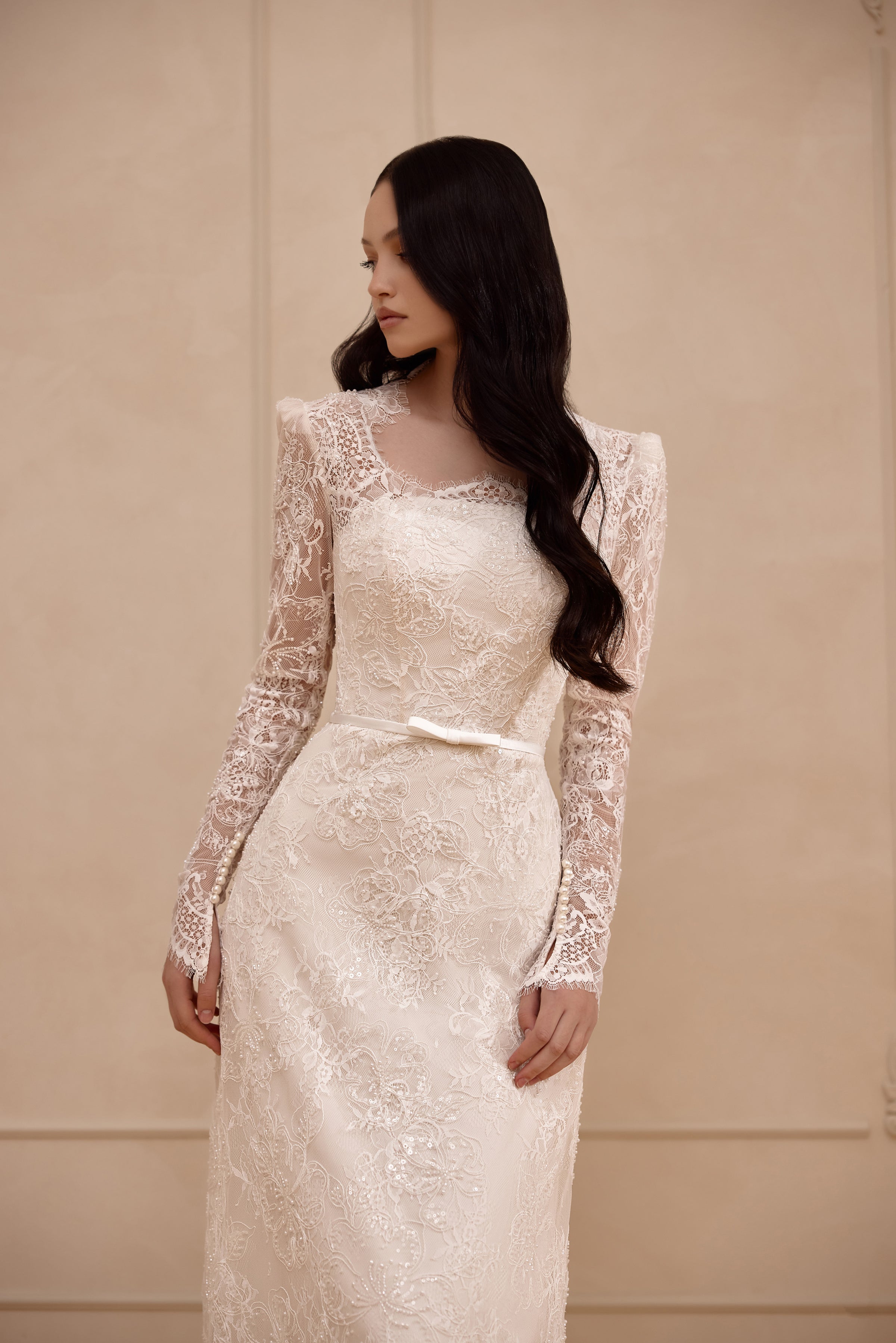 Close-up of an ivory wedding dress bodice with floral lace, sheer long sleeves, and a softly rounded neckline