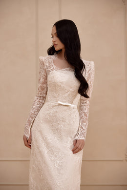 Close-up of an ivory wedding dress bodice with floral lace, sheer long sleeves, and a softly rounded neckline