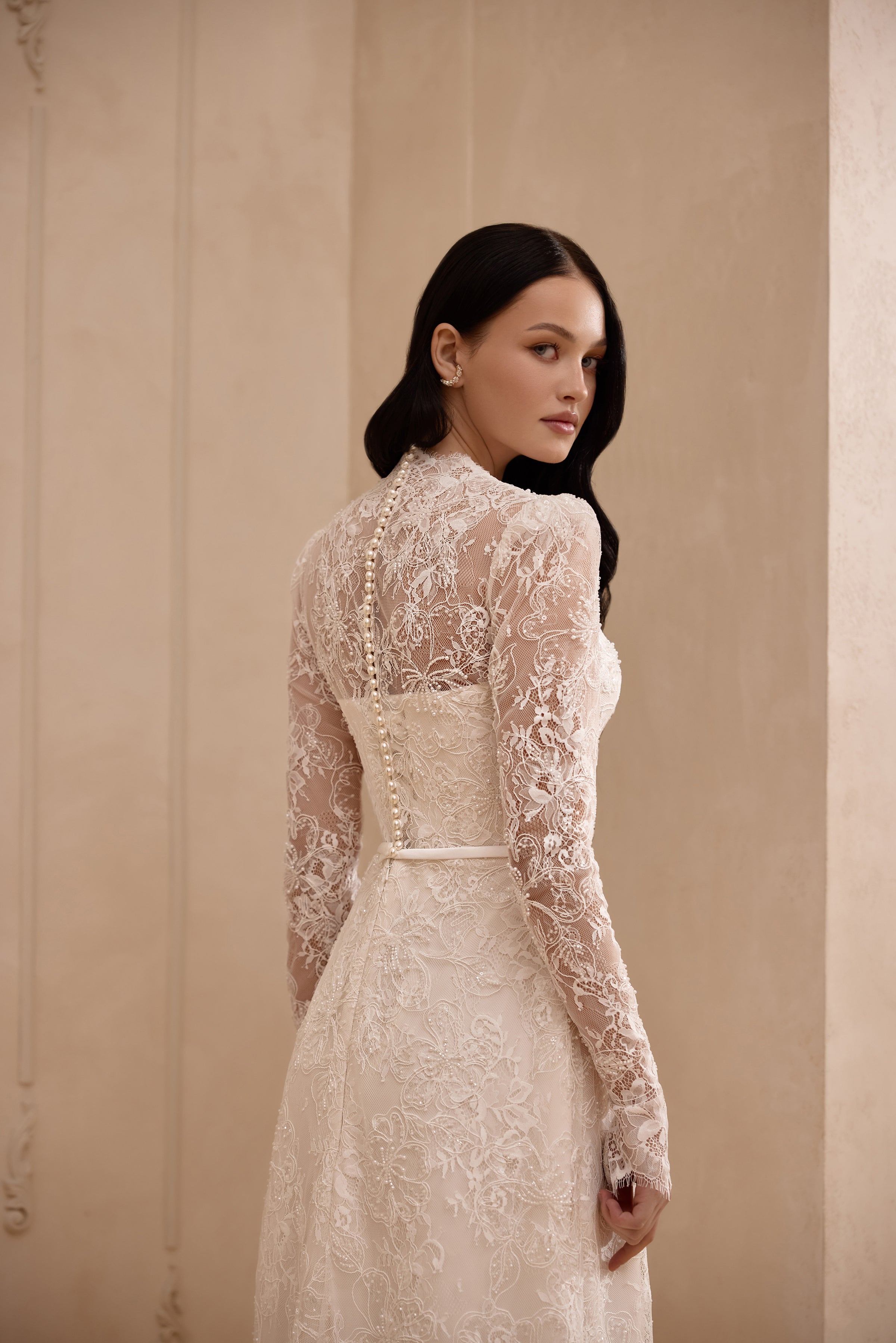 Three-quarter back view of an ivory lace wedding dress with a sheer illusion back and long sleeves