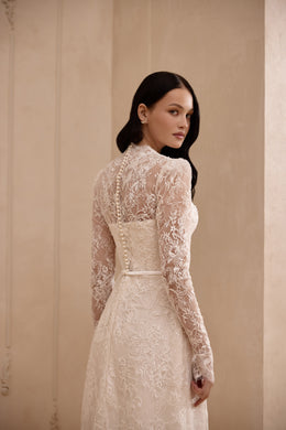 Three-quarter back view of an ivory lace wedding dress with a sheer illusion back and long sleeves